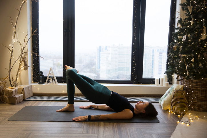 Woman doing yoga in a living room decorated with winter holiday items