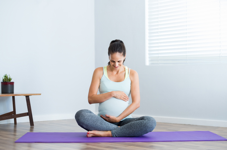 Pregnant woman sitting in lotus position on exercise mat and touching her belly. Pregnant athletic woman ready for yoga prenatal exercise. expectant mother relaxing at home.