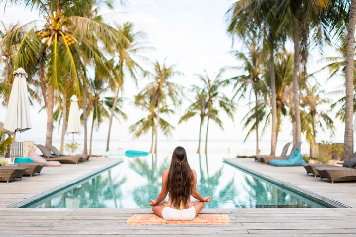 woman doing yoga at a pool with palm trees and a beautiful landscape