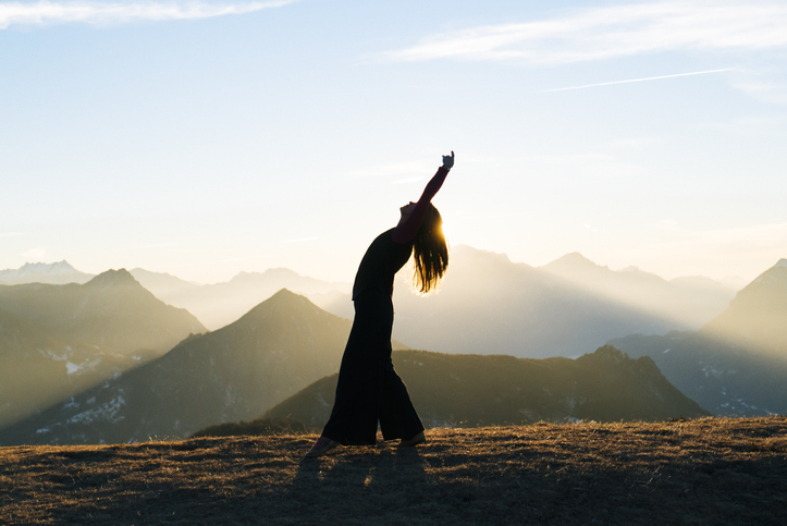 She is bending backwards as sun rises behind her. She is in an open meadow, Ticino Canton